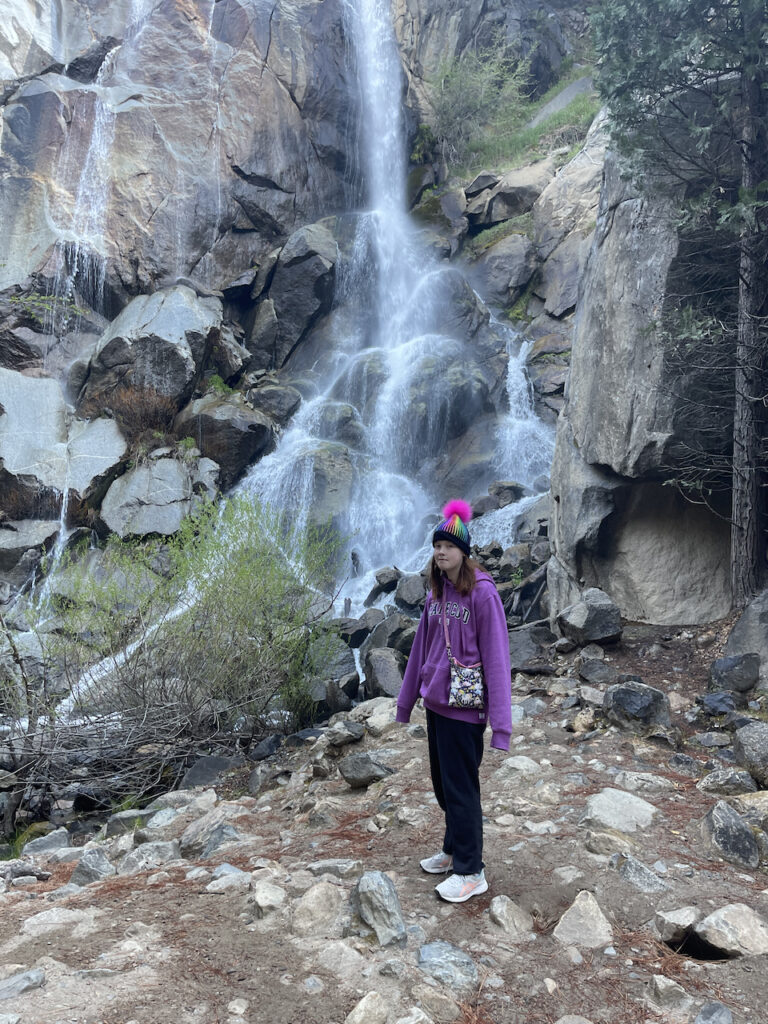 Cameron standing on the rocks in front of the Grrizzy Creek Waterfall in Kings Canyon National Park. It was cold, she is wearing a hat and sweatshirt. 