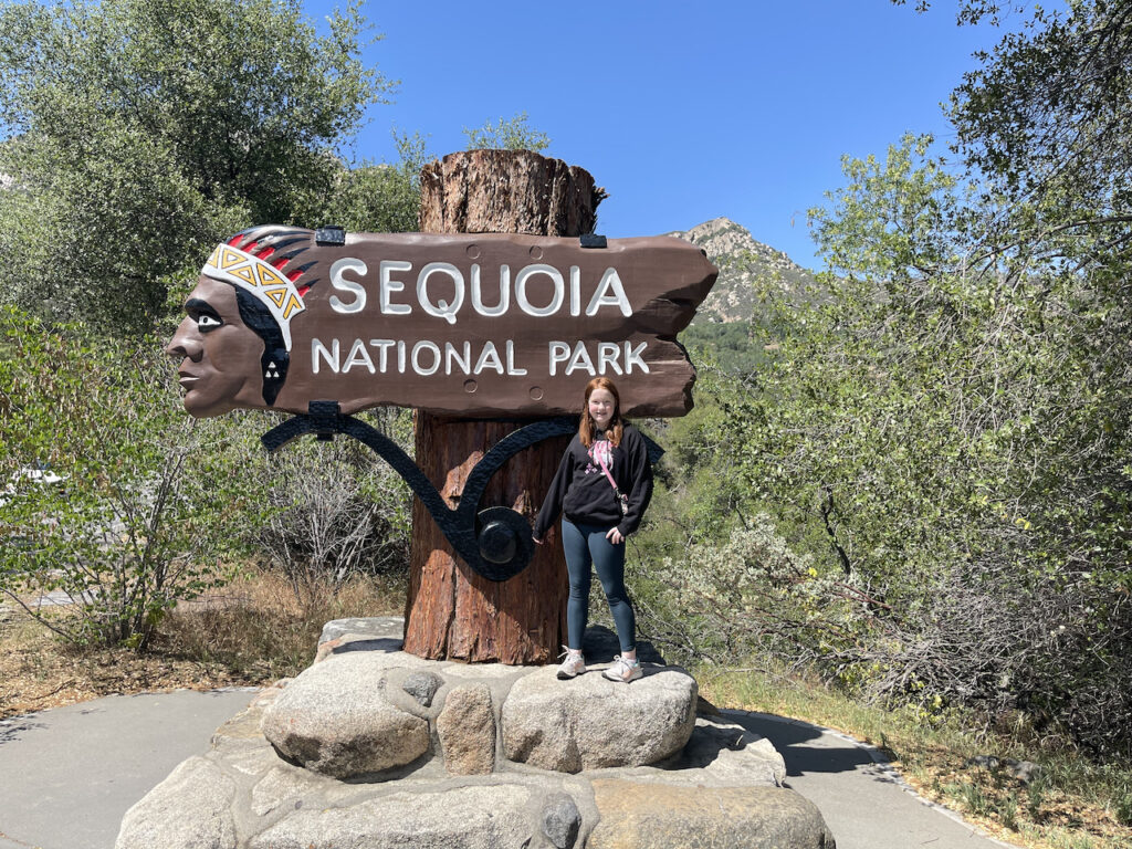 Cameron standing on rocks, in front of the Sequoia National Park Sign wearing leggins and a sweatshirt. 