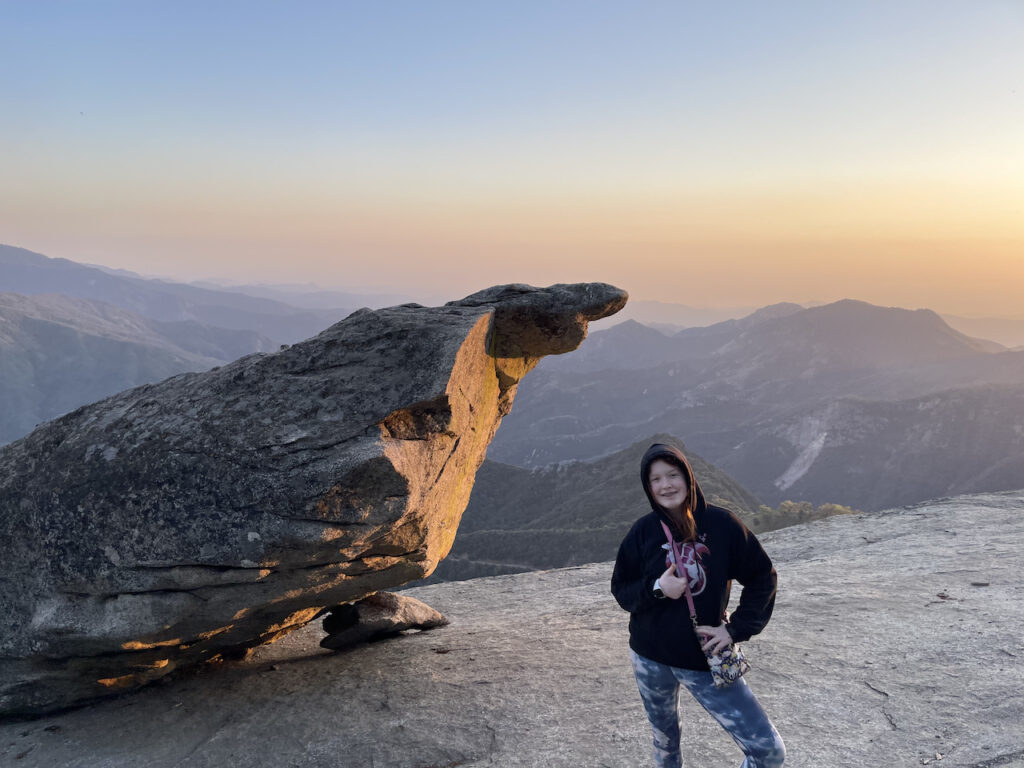 Cameron standing by Hanging Rock at Sunset, her hoodie was pulled up and the last bit of sun light was just hitting the rock face. The sky was turning orange and the valley below was falling into darkness.