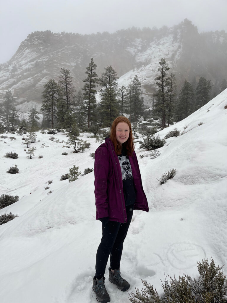 Cameron hiking in the falling snow in Zion National Park. Stopped for a minute she made a happy face in the snow, walking up a rather steep section of zion. In the background fog and clouds cover the near by mountains. 