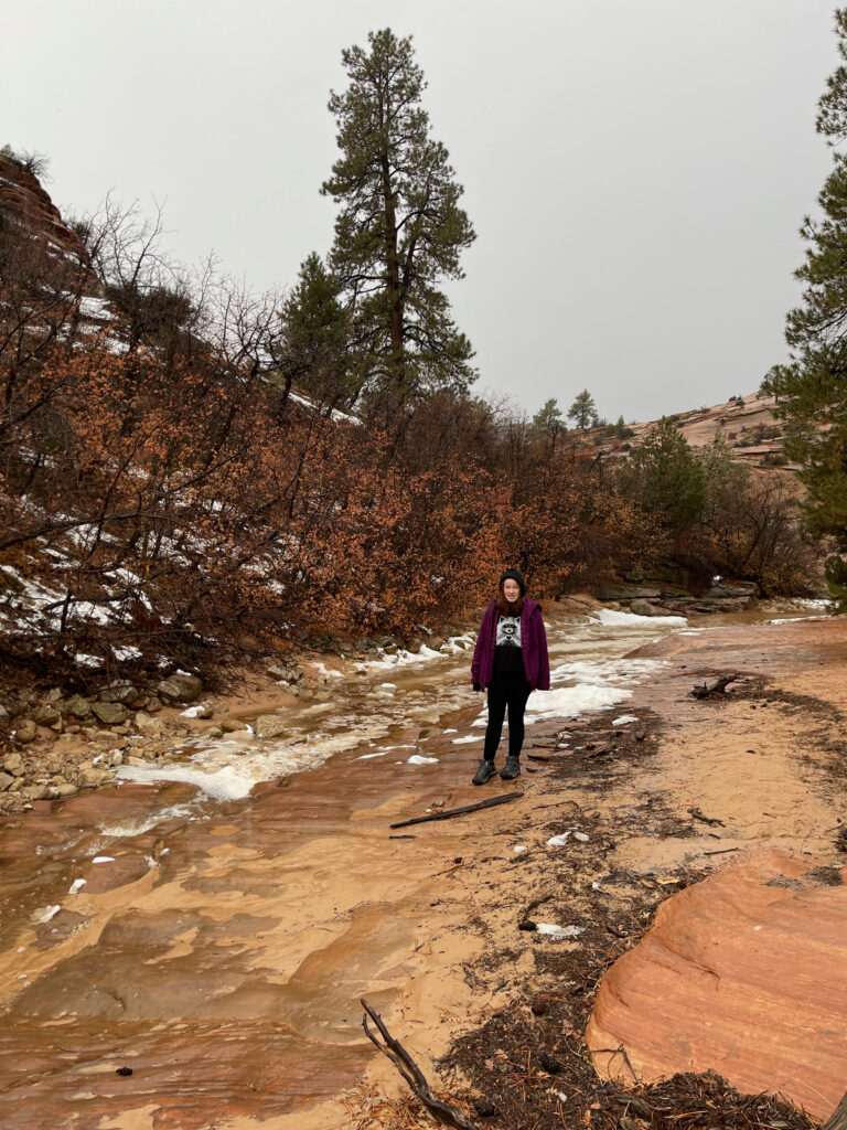 Cameron wearing her jacket standing in a small creek in the high country of Zion. The winter has frozen most of the water and ice is everywhere. 