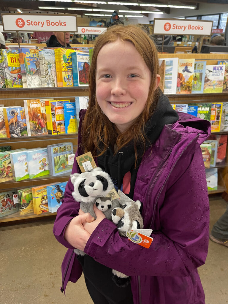 Cameron standing in a gift shop at Zion, holding three stuff animals with a massive grin on her face.