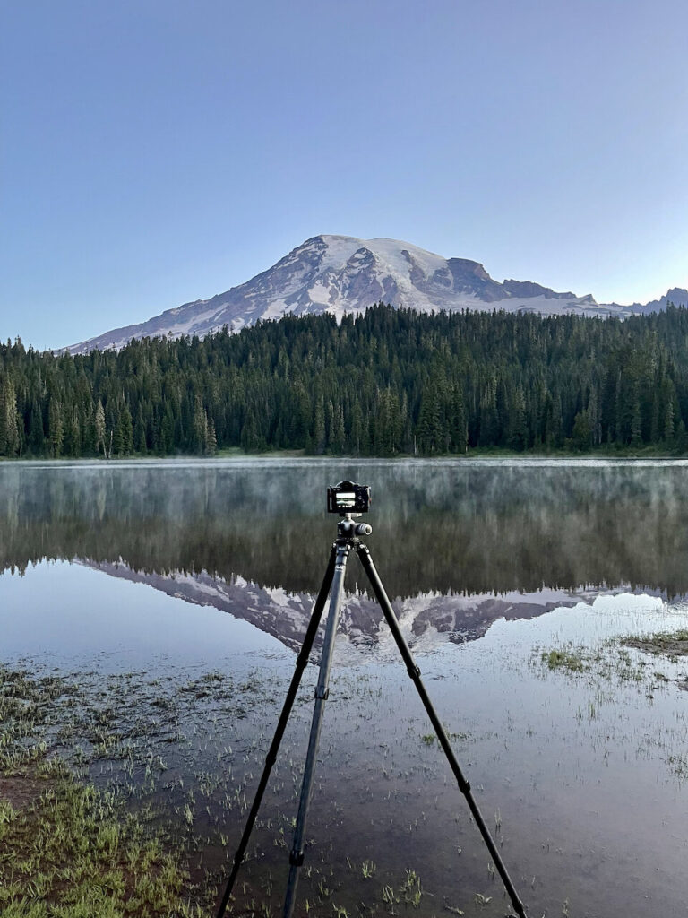 My camera on a tripod at Reflection Lake at Mount Rainier. The mountain is fully reflected int the water in front of me. 