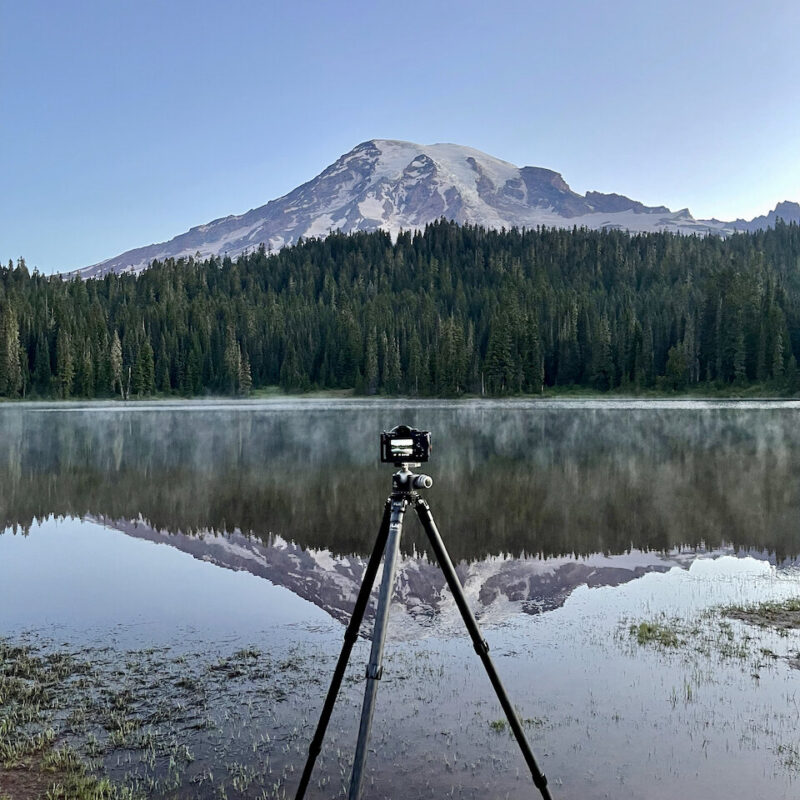 My camera on a tripod at Reflection Lake at Mount Rainier. The mountain is fully reflected int the water in front of me.