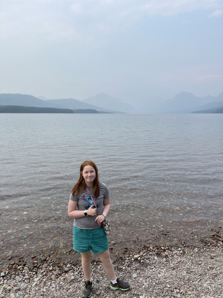 Cameron on the rocky shores of Lake McDonald with so much smoke in the air you can hardly make out the mountains across the lake in Glacier National Park.