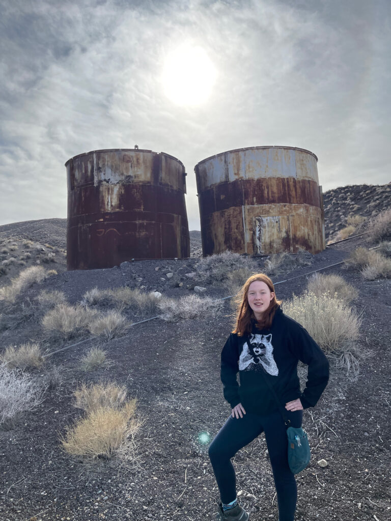 Cameron standing on a hill, next to old rusty tanks that where used for old mines in Death Valley National Park.