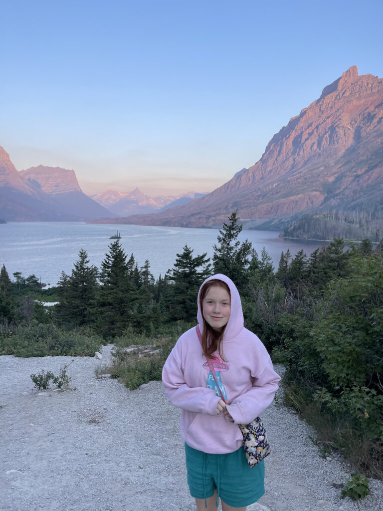 Cameron in shorts and hoodie very cold standing at a high overlook we found at Saint Mary Lake in Glacier National Park. The had just rises and the first light was hitting the mountains behind us. 