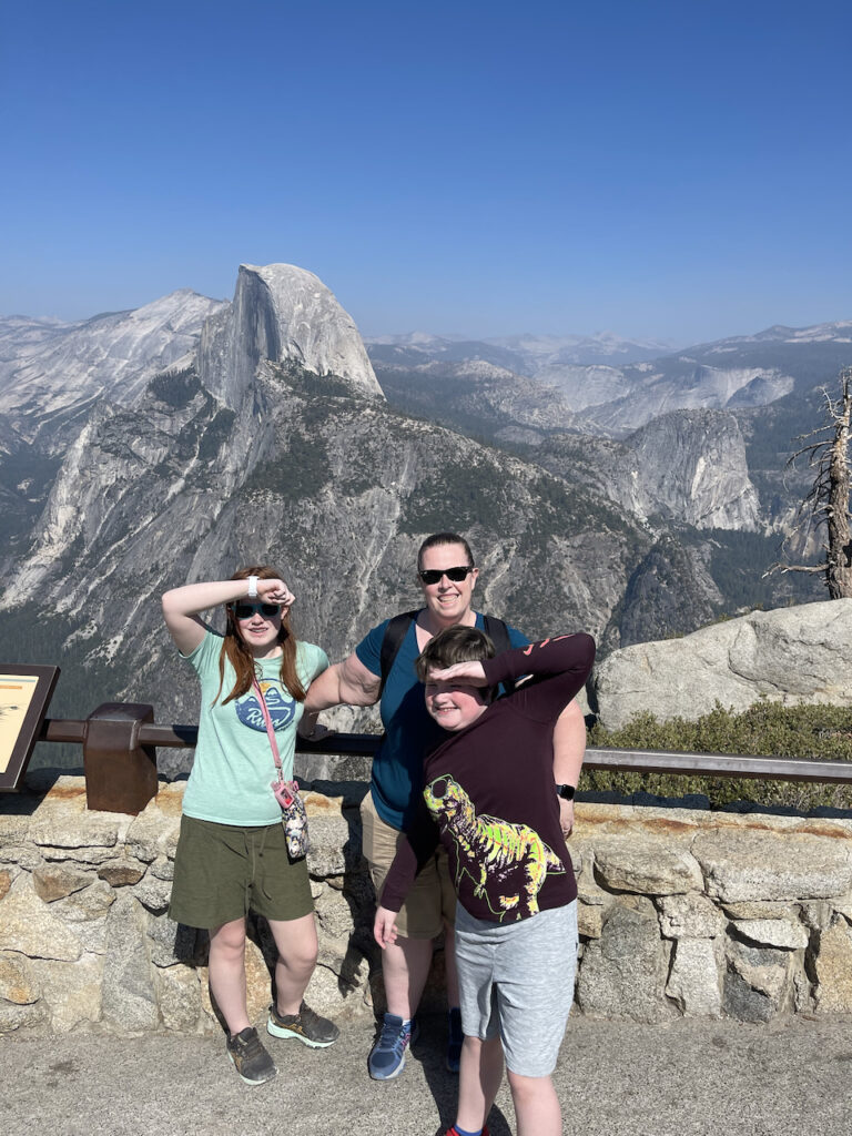 Cat, Collin and Cameron at Glacier Point overlook. Both kids are using their hands to block the strong mid day sun from their eyes. Half Dome can be seen right behind us. 