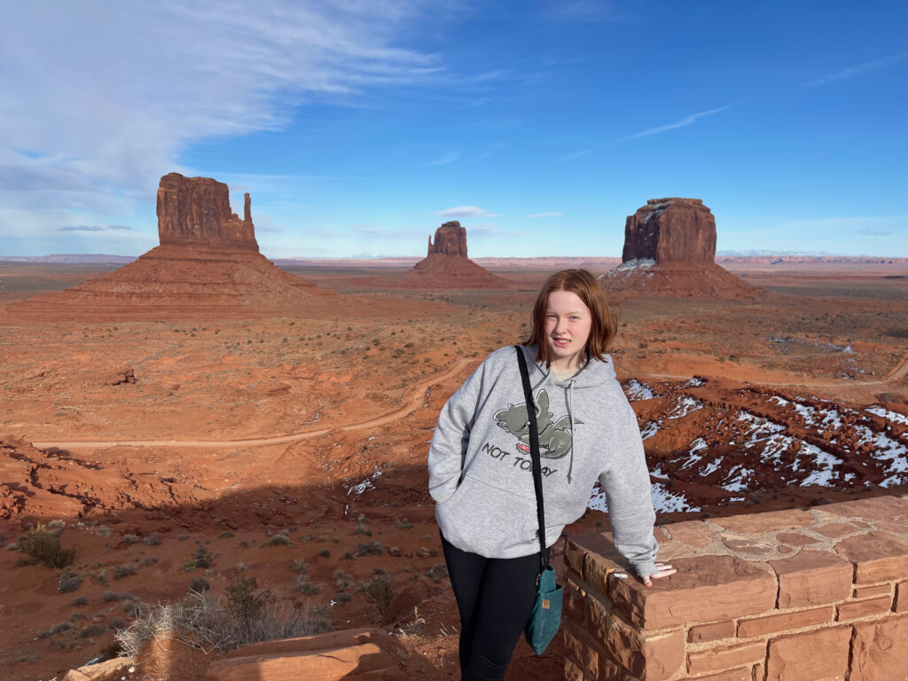 Cameron smiles as she stands by the rock wall at the overlook to Monument Valley.