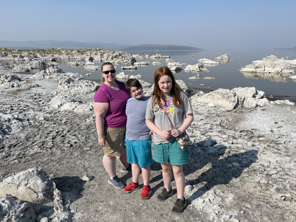 Cat, Collin and Cameron standing on the rocky shores of Mono Lake in the Eastern Sierra. You can see the white Tufas behind them but the haze and smoke almost blocks the mountain view across the lake.