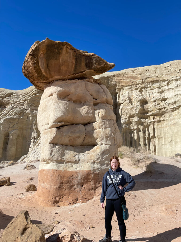 Cameron wearing a hoodie and standing in front of a massive Hoodoo with a bright blue sky in the background.