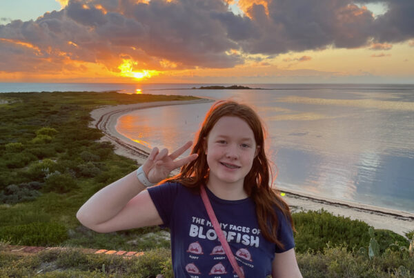 Cameron at sunset standing on top of Fort Jefferson in Dry Tortugas National Park. There is an amazing sunset over the ocean just behind her, with the clouds lit up with color.