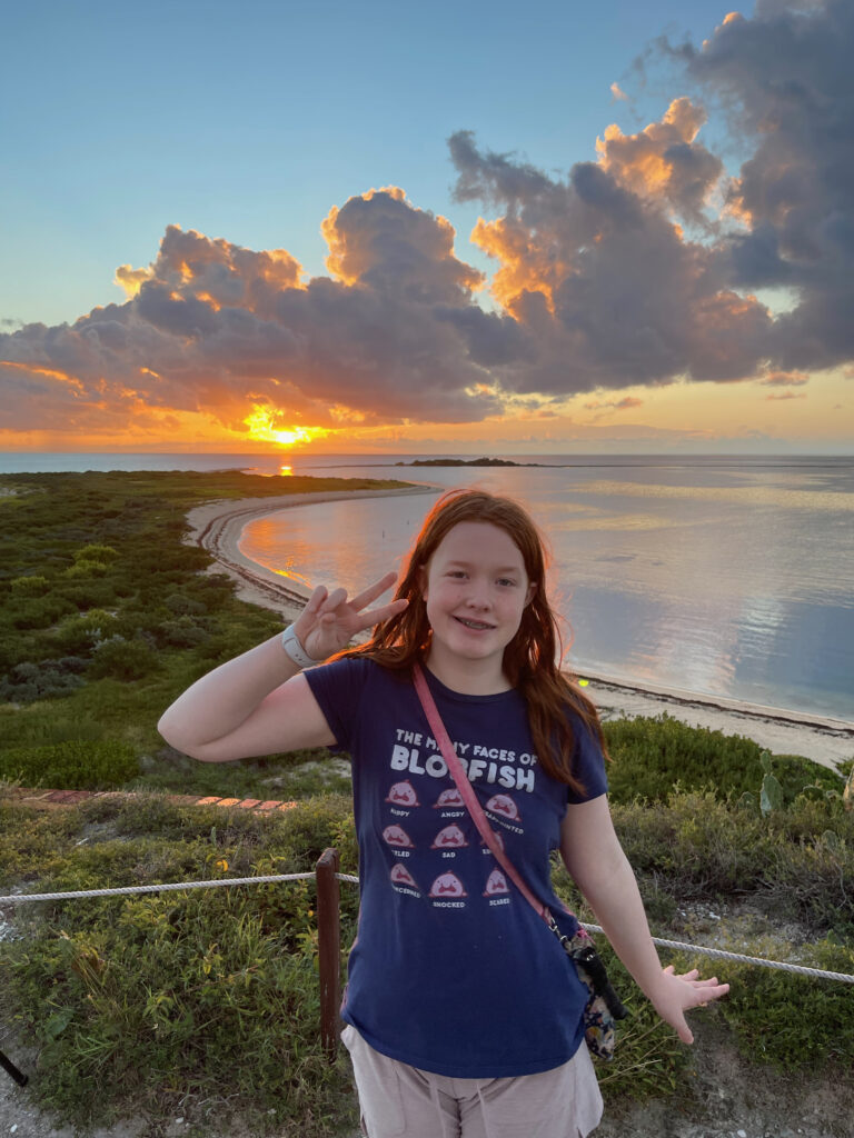 Cameron at sunset standing on top of Fort Jefferson in Dry Tortugas National Park. There is an amazing sunset over the ocean just behind her, with the clouds lit up with color.