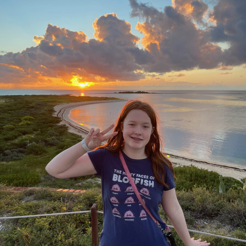 Cameron at sunset standing on top of Fort Jefferson in Dry Tortugas National Park. There is an amazing sunset over the ocean just behind her, with the clouds lit up with color.