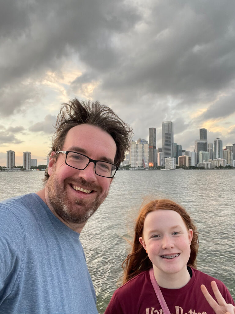 Cameron and myself standing near the water off the Rickenbacker Causeway with the Miami skyline in the background. Cami has a big smile and is making a peace sign and my hair is a mess from the wind.