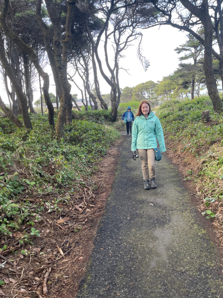 Cameron wearing her raincoat and carrying my tripod and Collin behind her walking down the trail to Seal Rock.