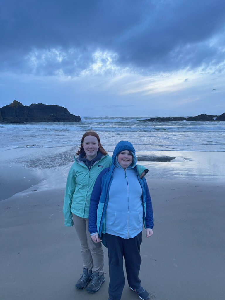 Collin and Cameron standing in their rain gear on the beach at Seal Rock State Recreation area.  Rain and storm clouds hang over the ocean behind them.