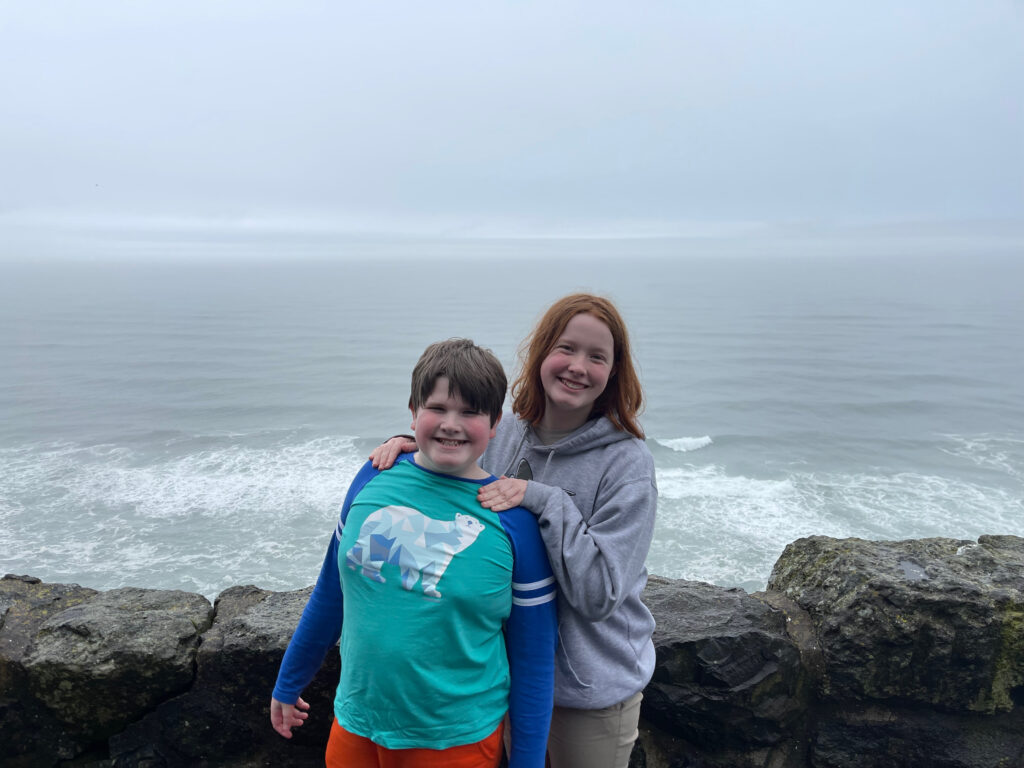 Cameron and Collin smiling and standing by a rock wall, overlooking the Pacific Ocean on a very foggy day near Sea Lion Point.