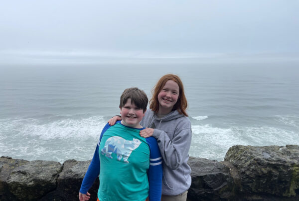 Cameron and Collin smiling and standing by a rock wall, overlooking the Pacific Ocean on a very foggy day near Sea Lion Point.