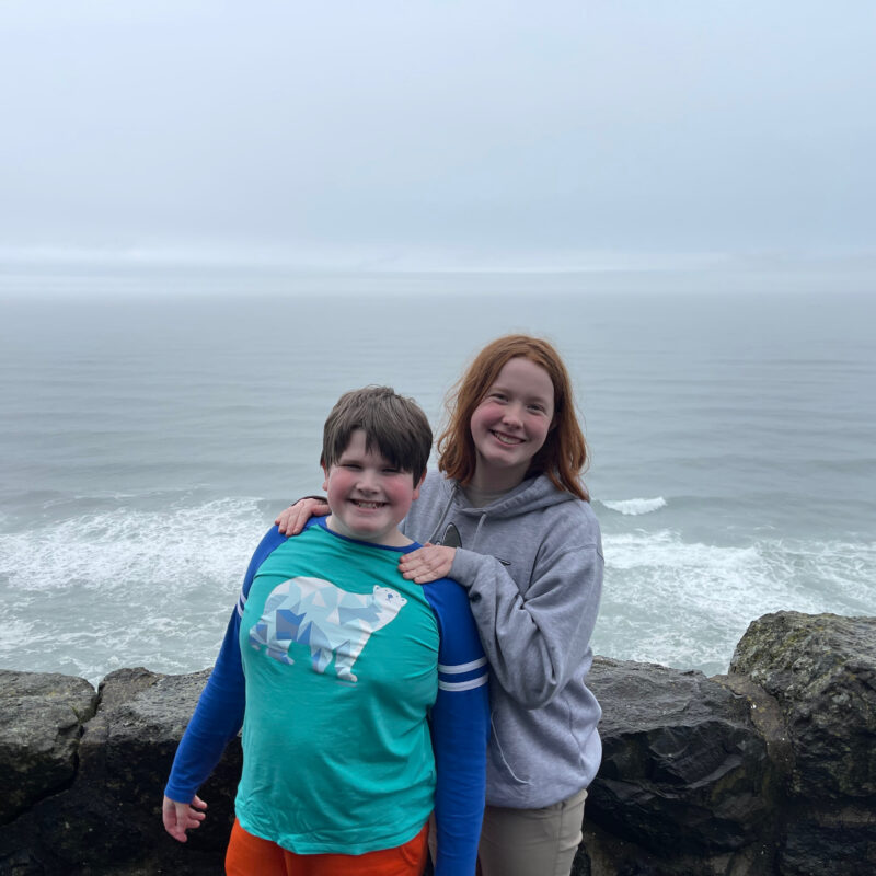 Cameron and Collin smiling and standing by a rock wall, overlooking the Pacific Ocean on a very foggy day near Sea Lion Point.