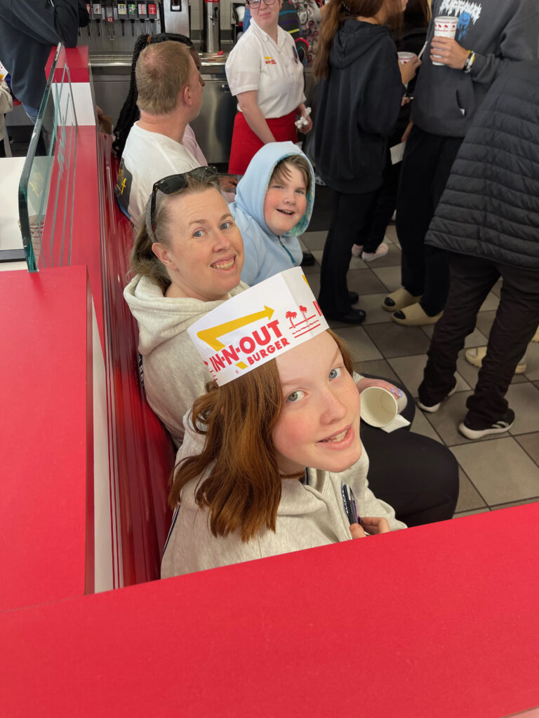 Collin, Cat, and Cameron who is wearing an In-N-Out hat, sitting on the bench waiting for our lunch at In-N-Out.