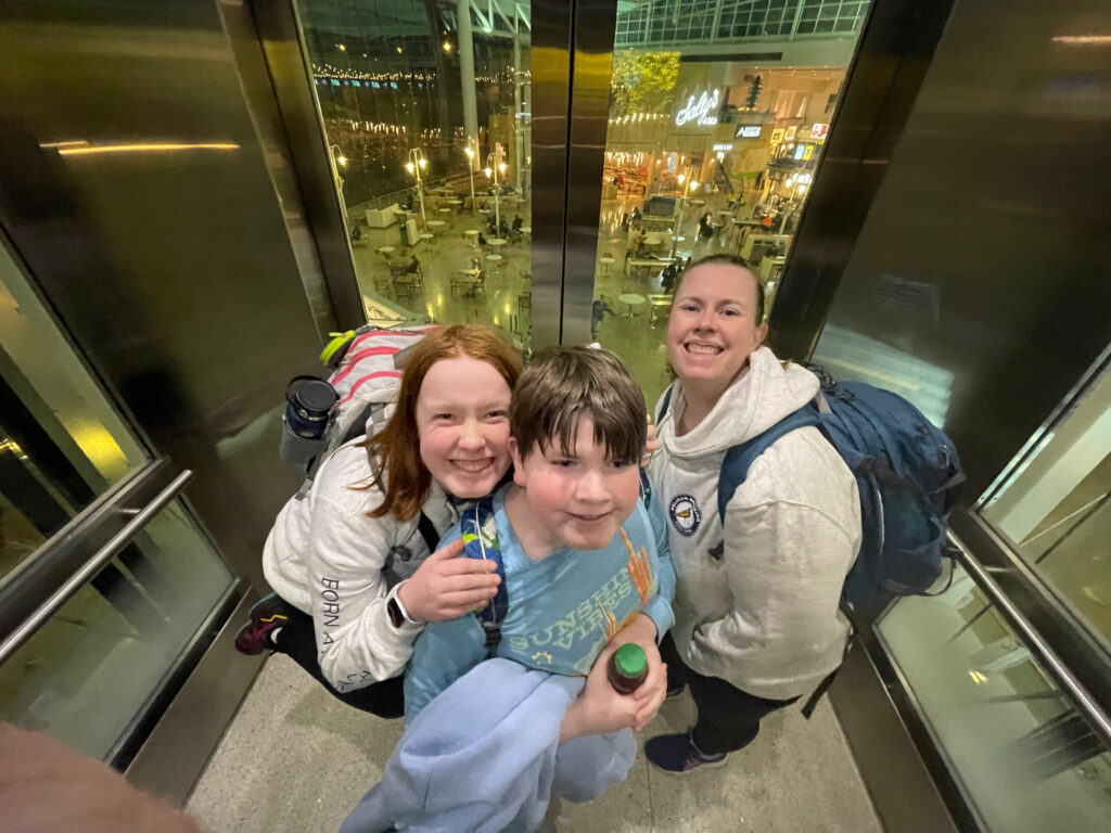 Cat, Cameron and Collin in the elevator in the Seattle Airport, all smiles, all wearing backpacks on the way up to the lounge. 