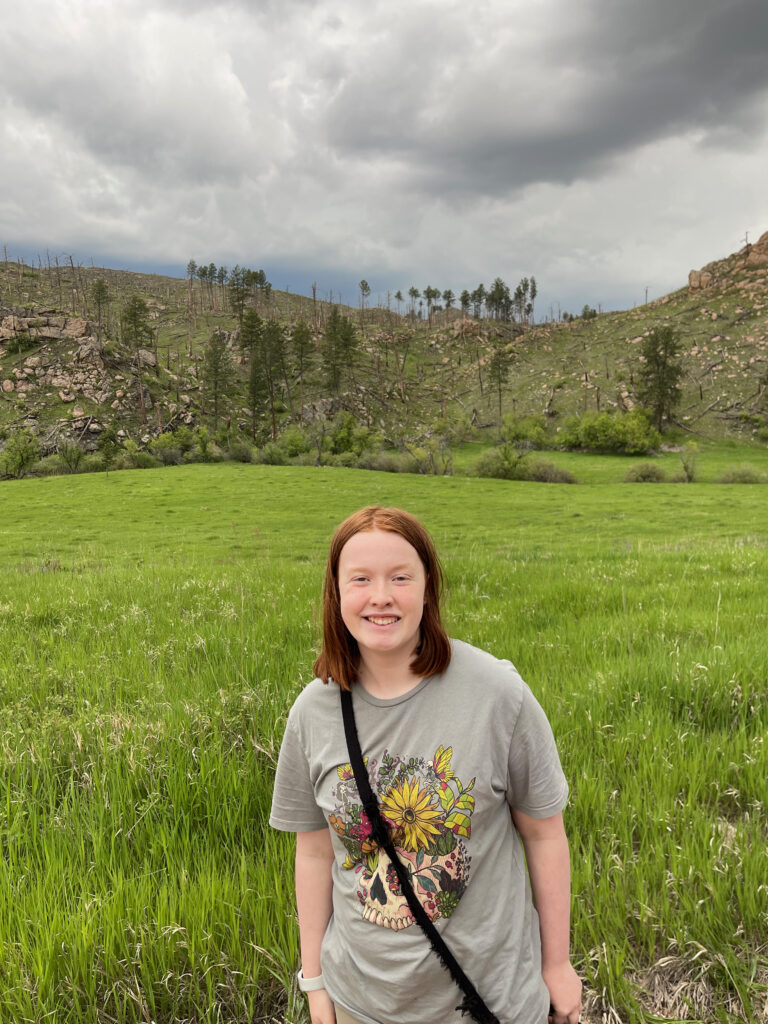 Cameron in the middle of a field near wind cave national park, trees and hills are in the background.