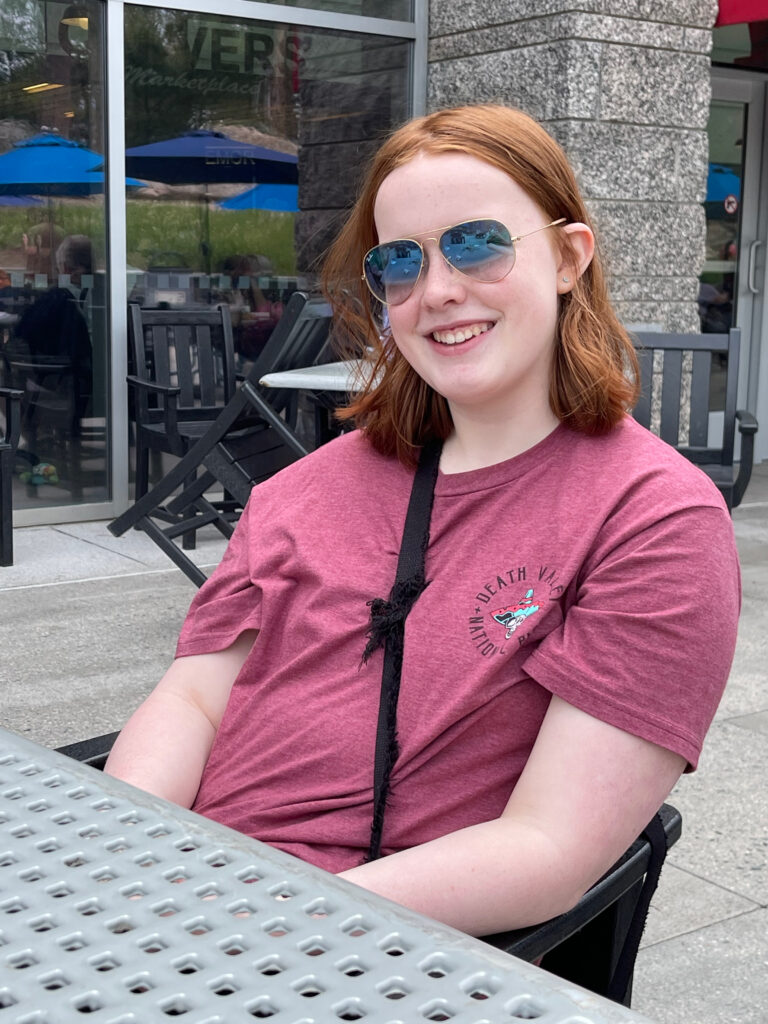 Cameron sitting at a table on the patio at Mount Rushmore. Wearning a Death Valley T-shirt and sunglasses. 