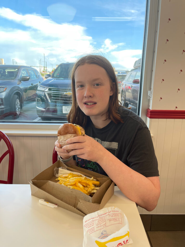 Cameron eating a Double-Double at In-N-Out burger sitting inside at a table.