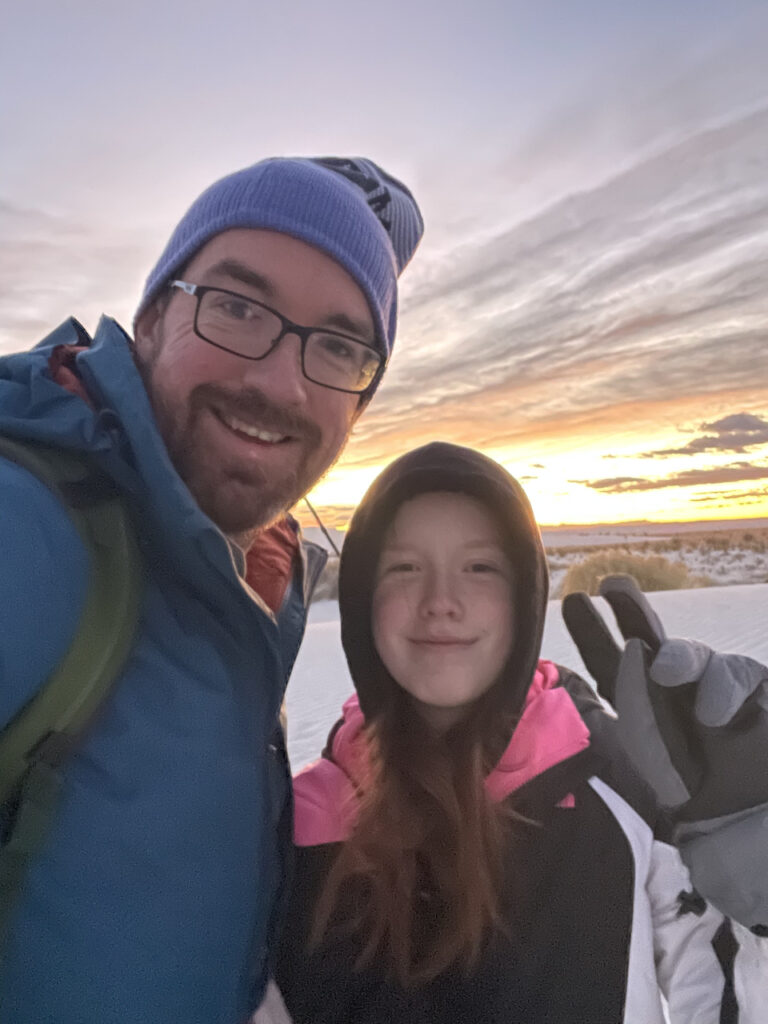 Cameron making a peace sign and myself, at sunrise in White Sands. Both of us wearing winter gear for the freezing morning but the sky is full of clouds and color.