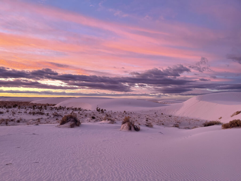 A stunning photo of a winters sunrise in White Sands National Park. The white sand turned purple in the morning light. The layers of clouds took on colors from deep purple to bright red.