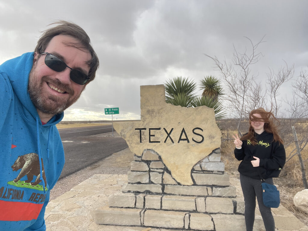 Cameron and myself with our hair being blown but the strong winds, standing in front of the Texas sign on the National Parks Highway.