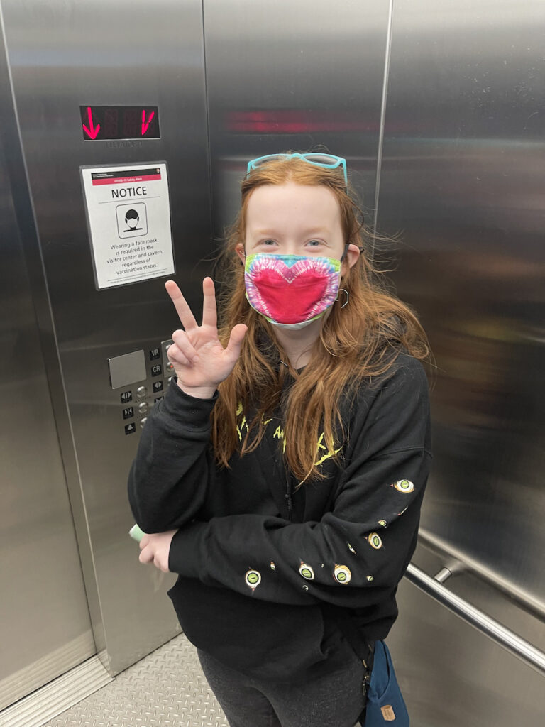 Cameron wearing a face mask in the elevator making a peace sign going into the caves at Carlsbad Caverns.