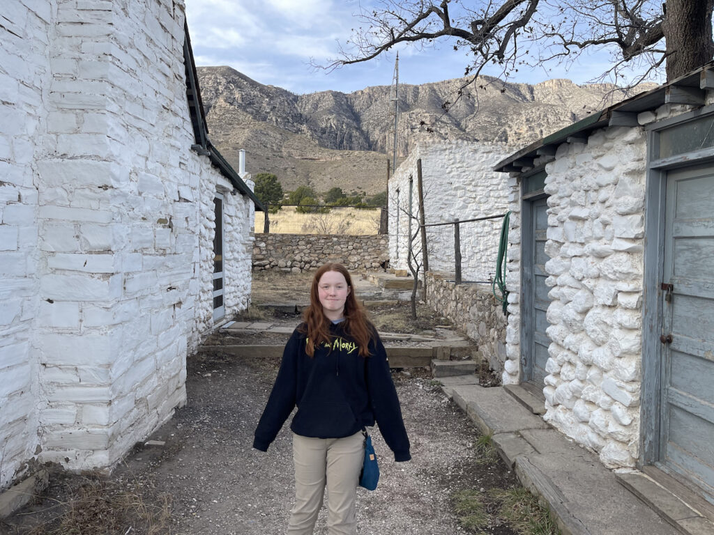 Cameron standing between two old white brick buildings in Frijole Ranch.