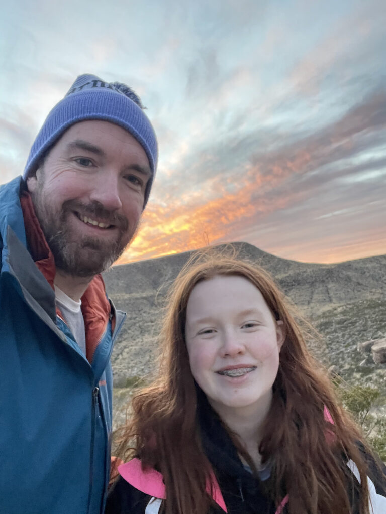 Cameron and myself smiling at sunset with a wonderful red and yellow sky above us in the mountains. 