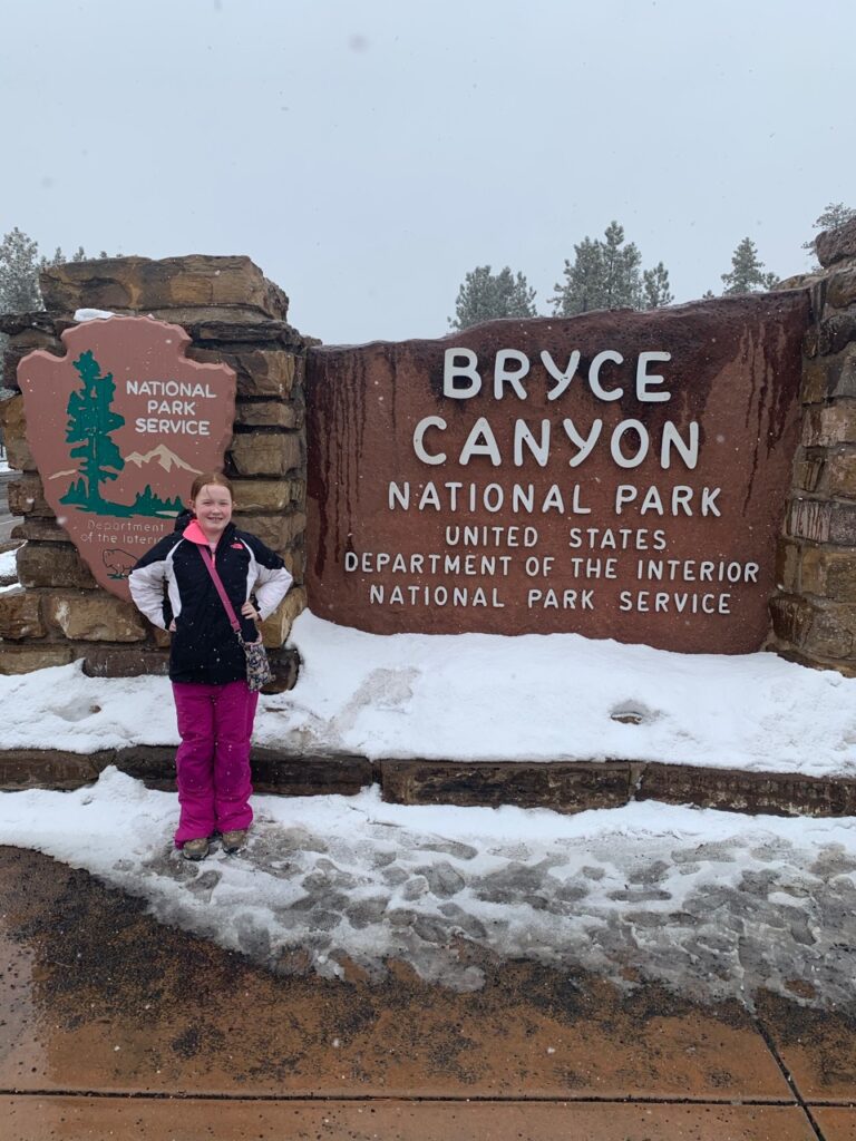 Cameron in front of the Bryce Canyon National Park sign in the snow.