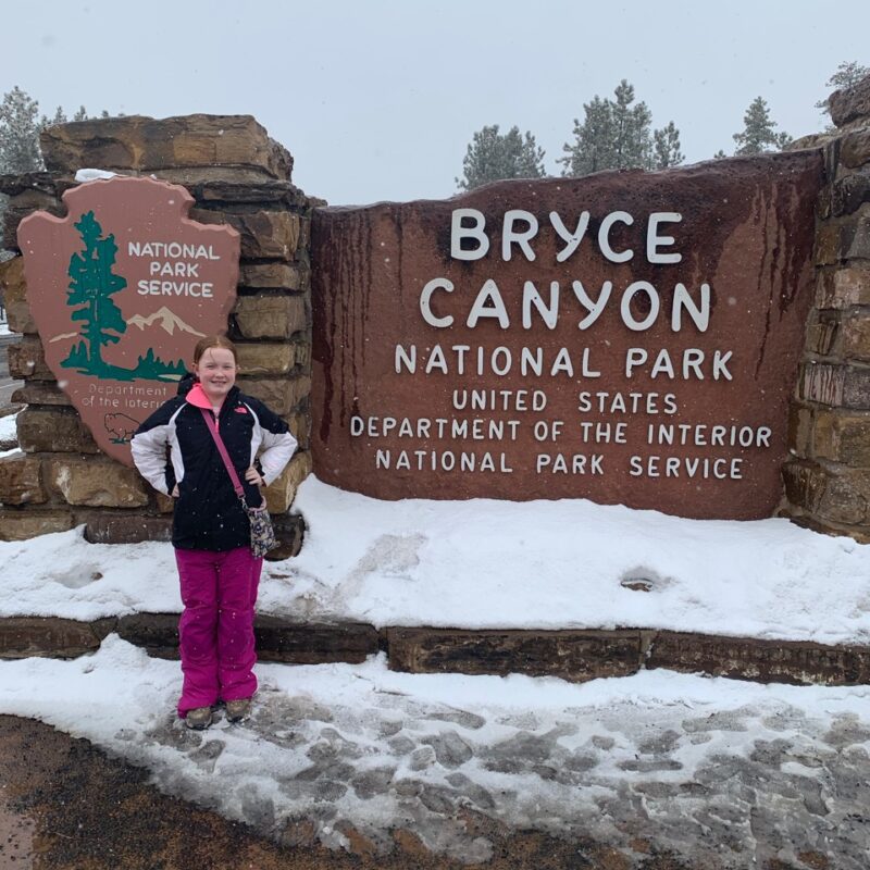 Cameron in front of the Bryce Canyon National Park sign in the snow.