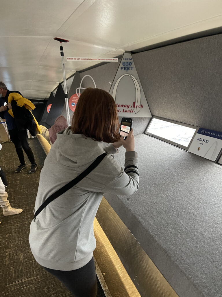 Cameron taking a photo with her phone through the small window at the very top of the Gateway Arch.