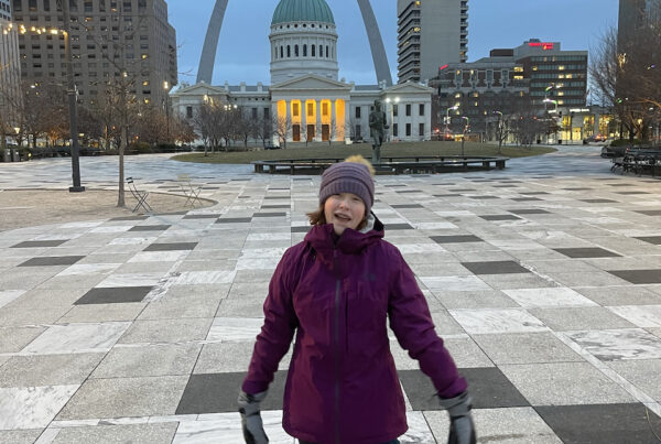 Cameron at sunrise in a hat, gloves and hat, in the pre-dawn hours in Kiener Plaza with the Gateway Arch and State house in the background.