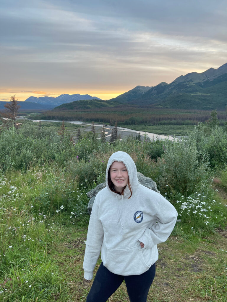 Cameron standing in a filed near the savage river, the clouds have turned yellow over the mountains in the distance.