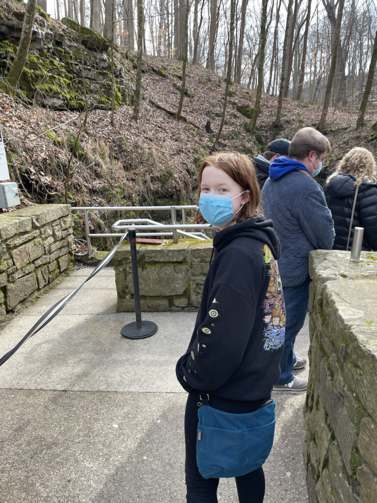 Cameron outside wearing a face mask making he way around the stone walls and down the walkway to the entrance to the cave.