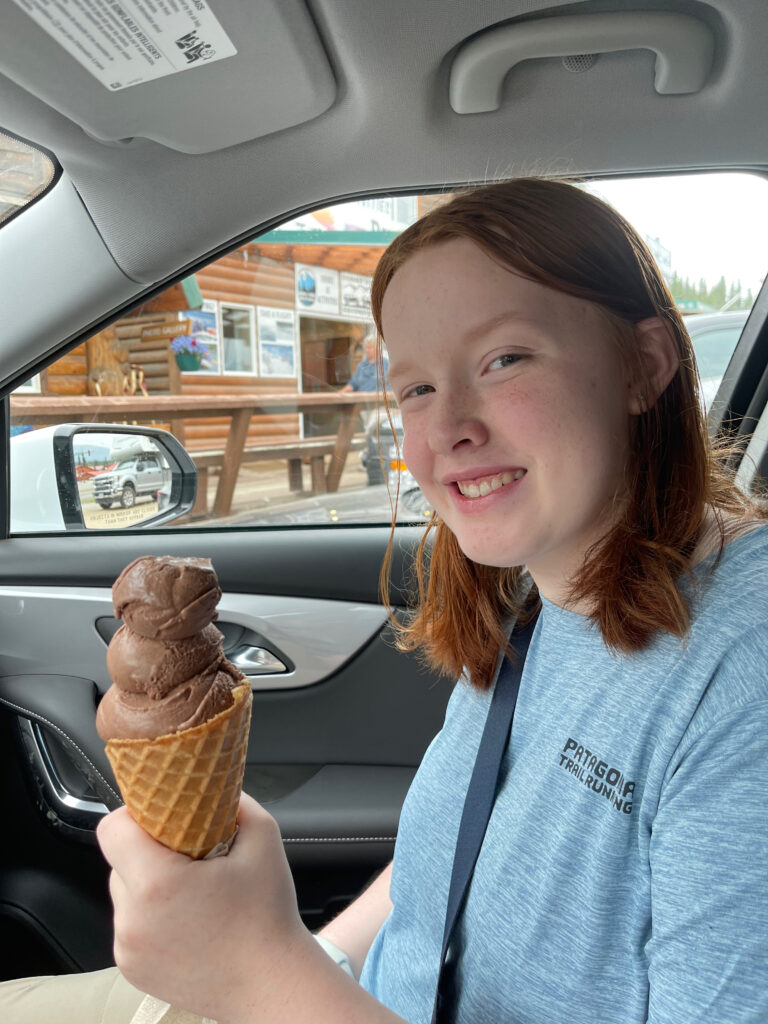 Cami sitting in the front seat of the car, smiling and holding up her large ice cream cone. After a stop at the Denali Glacier Scoops Ice Cream stand.