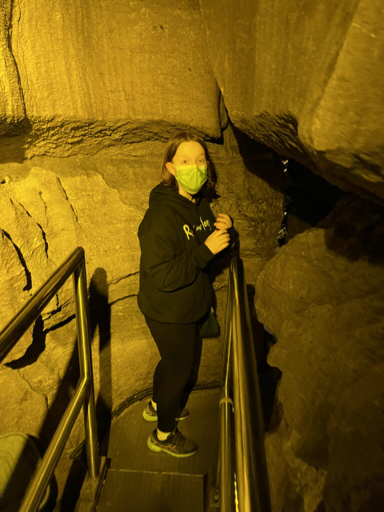 Cami standing on top of a platform making her way into the Mammoth Cave. The only light is very yellow this deep in the cave.