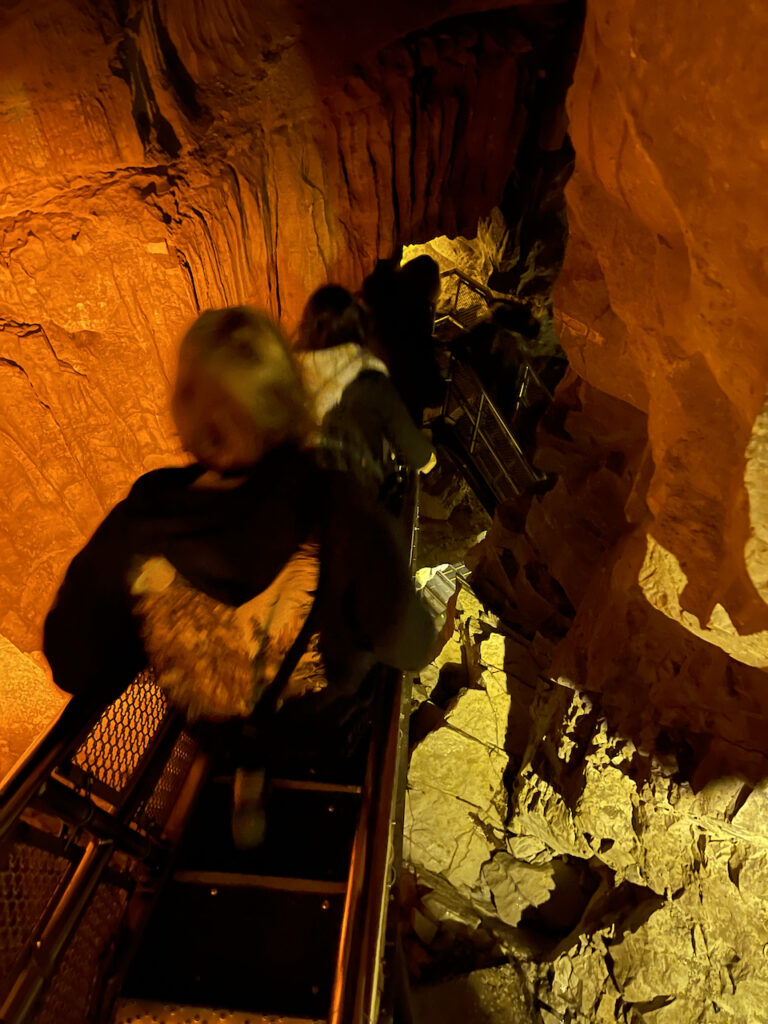 Cameron making he way down the steep and old stairs that bring you into the lower parts of the cave. There is a log jam of people in the dim light being very careful on these stairs.