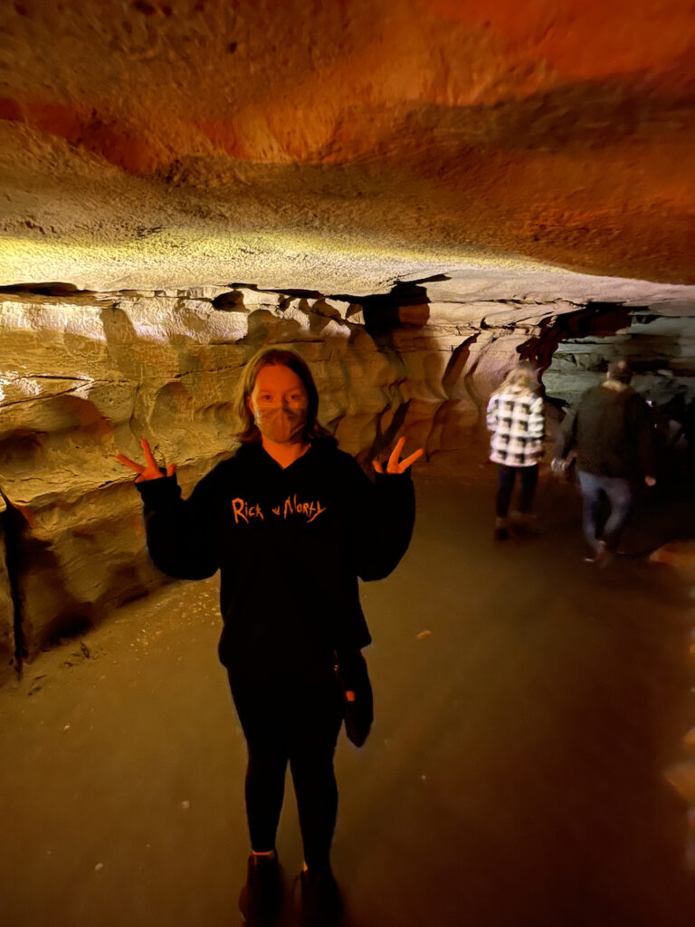 Cami wearing a mask and making a double peace sign deep in the cave. This is taken in a wider passage way, taken on a tour with other people around.