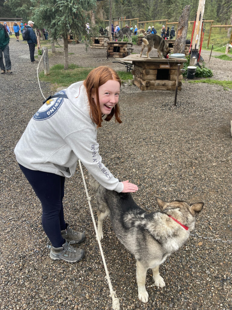 Cameron outside wearing a sweatshirt and a big smile, petting one of the sleds dogs in Denali. 