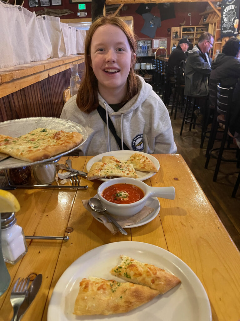 Cameron sitting at a high top bar table wearing a sweatshirt and her long red hair. Inside Prospectors Historic Pizzeria and Alehouse. The table if full of food.