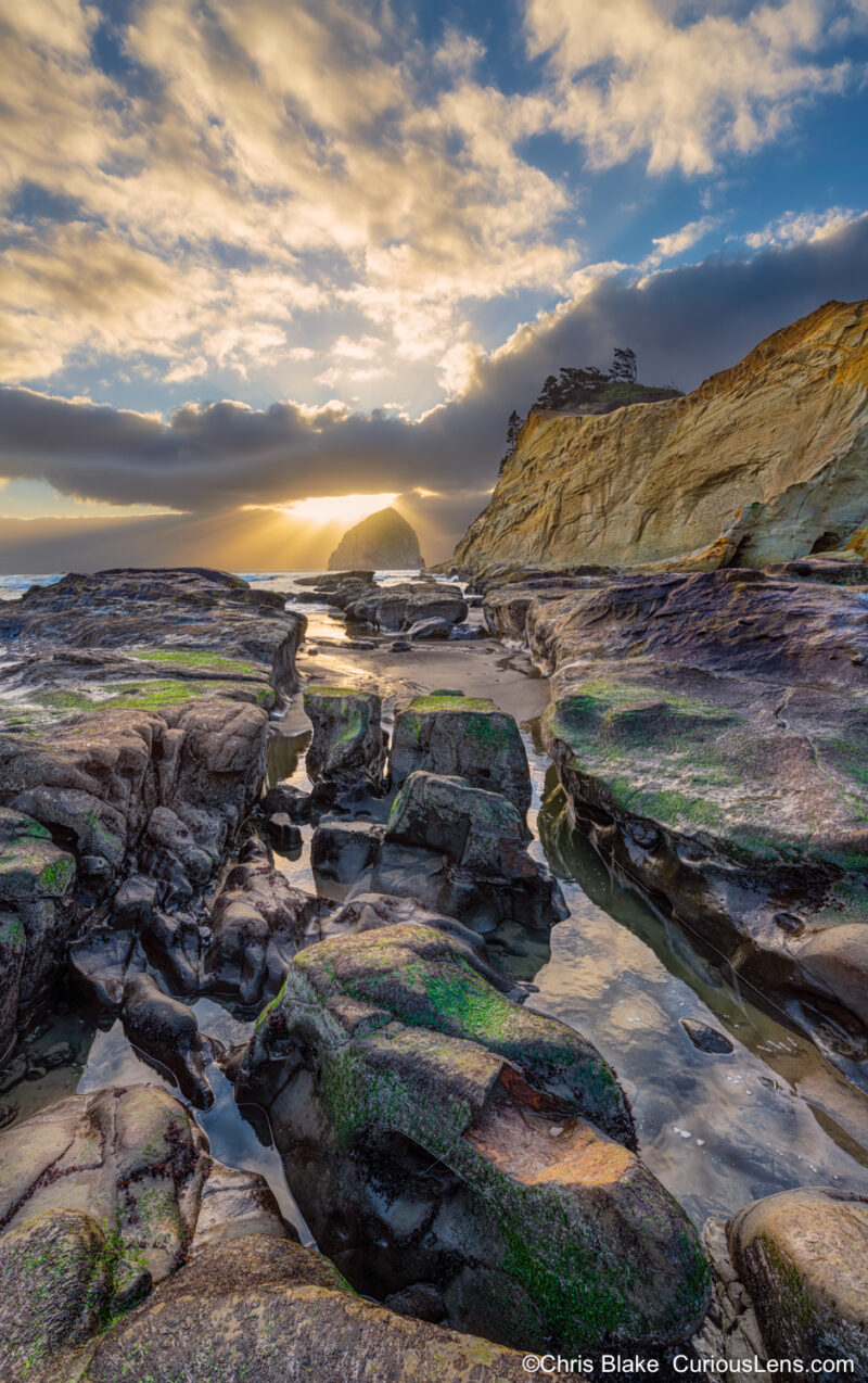 Sunset at Cape Kiwanda with sun above Chief Kiawanda Rock, sandy beach, rock formations, sandstone cliffs, and tide pools.