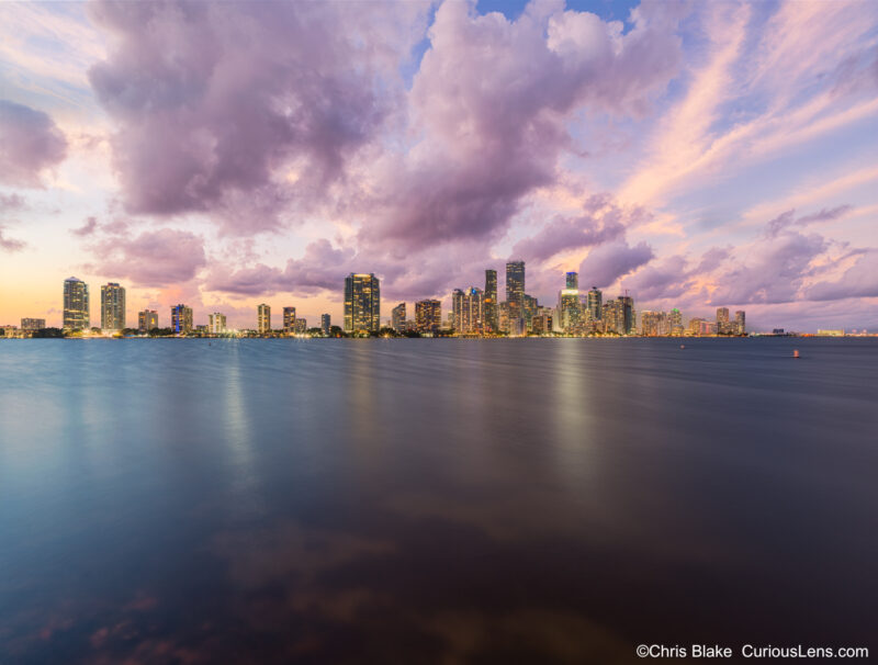 Downtown Miami skyline from Hobie Island with Villa Regina, Palace Condominium, Four Seasons, storm clouds, sunset, and city lights.