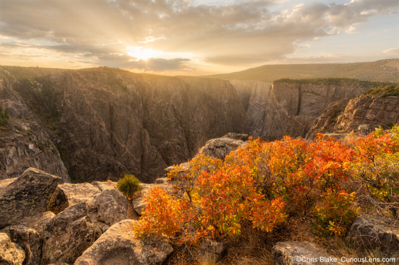 Black Canyon of the Gunnison at sunset from north rim with steep walls, narrow river, vibrant sky, and rugged terrain.